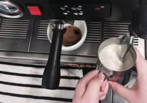 Close-up of barista frothing milk while making coffee