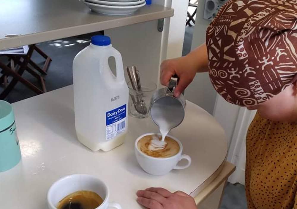 Trainee barista creating shape on top of coffee while pouring milk as she prepares to serve it